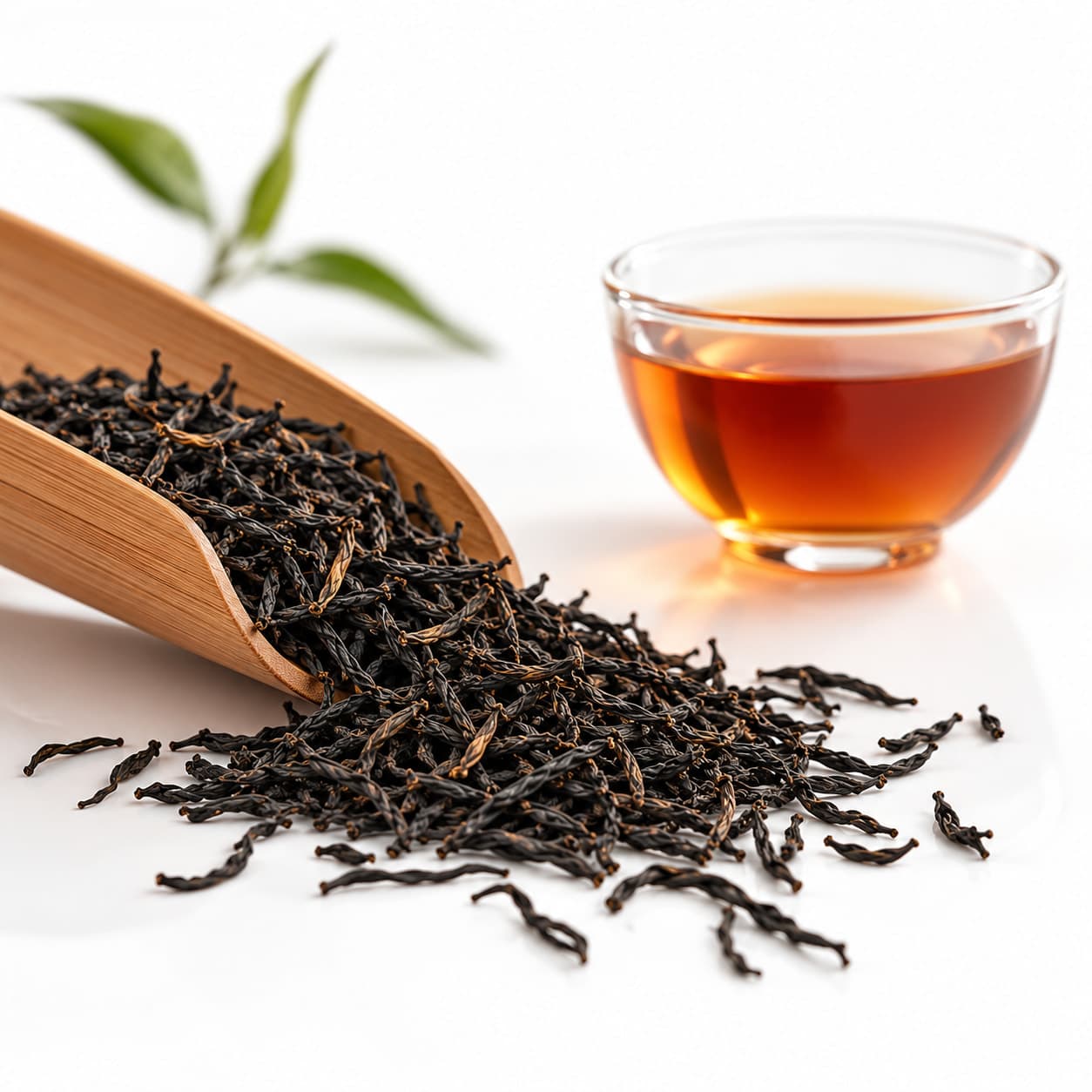 Wuyi black tea spilling from a bamboo scoop beside a glass cup of amber tea.
