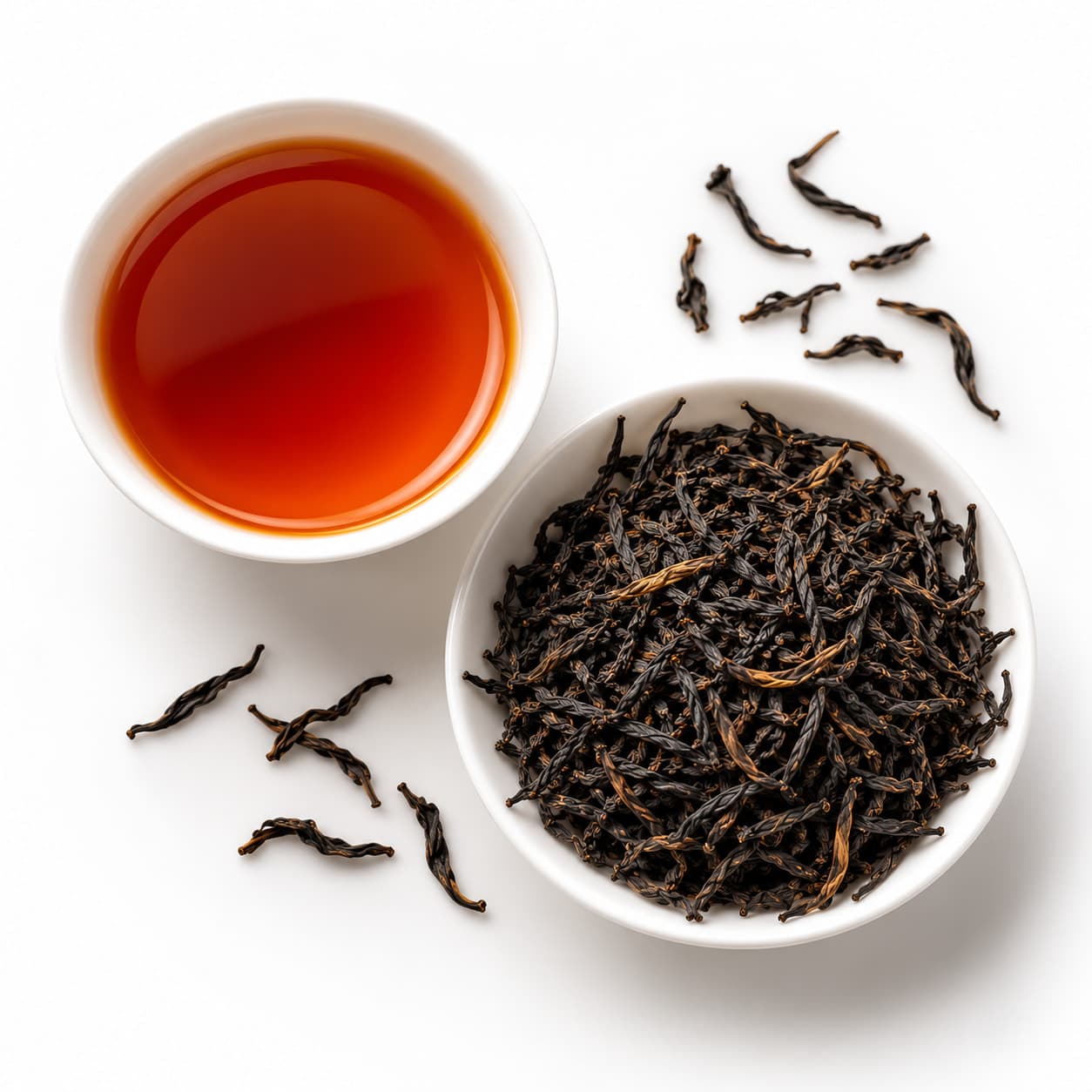 Seen from above: a cup of deep amber black tea beside a bowl of dark, twisted leaves.